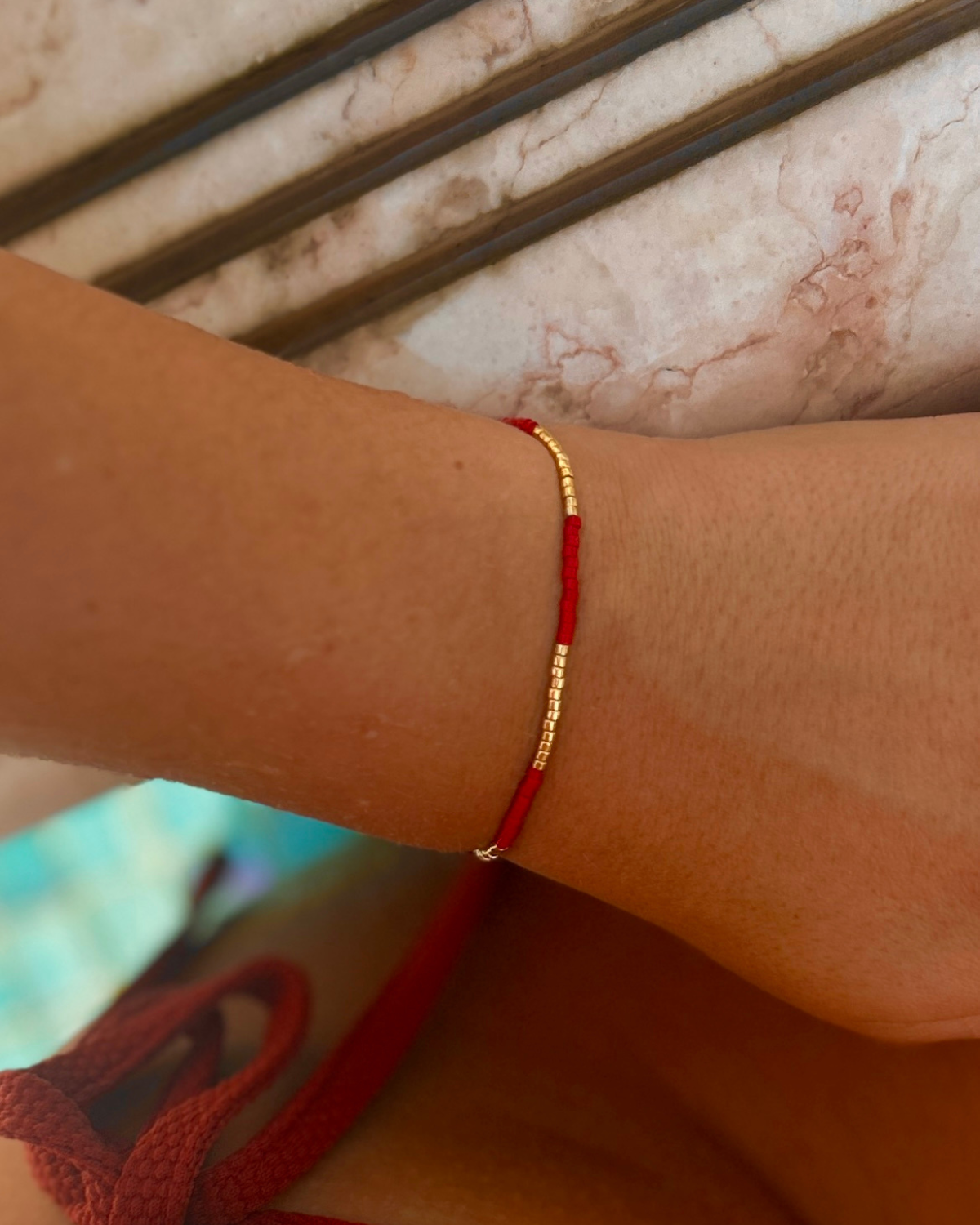 Red bracelet on a wrist styled with a Tucca Swim bikini