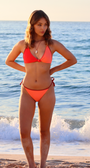 Woman in an orange bikini standing on a beach with ocean waves in the background