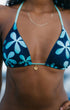A close-up of a woman wearing a dark navy bikini top with a light blue and turquoise floral pattern, featuring a small gold flower charm at the center.