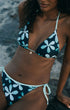 A woman wearing a two-piece bikini with a dark navy background and a light blue and white floral pattern, photographed outdoors against a rocky, blurred background.